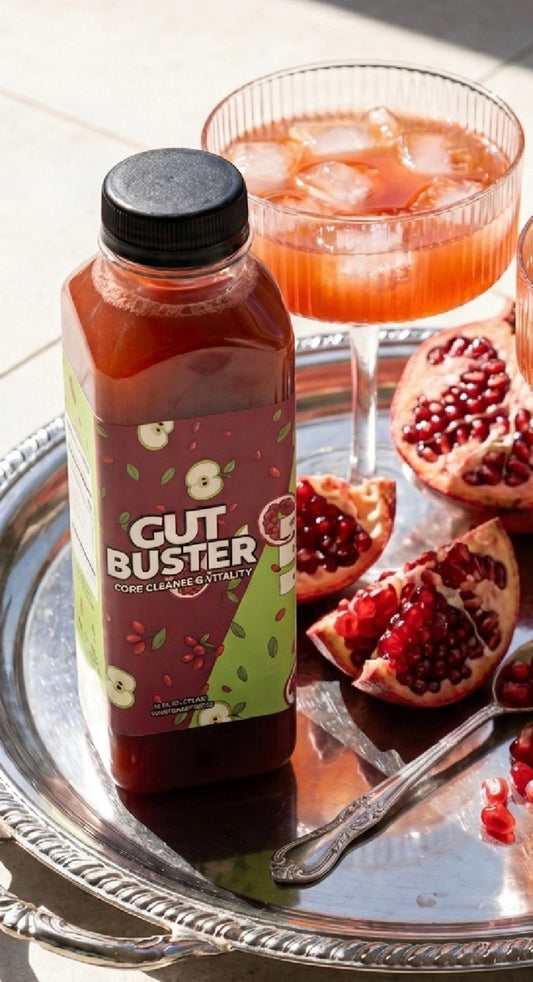 Gut Buster gut-support drink bottle on a silver tray with a pomegranate cocktail and fresh pomegranate